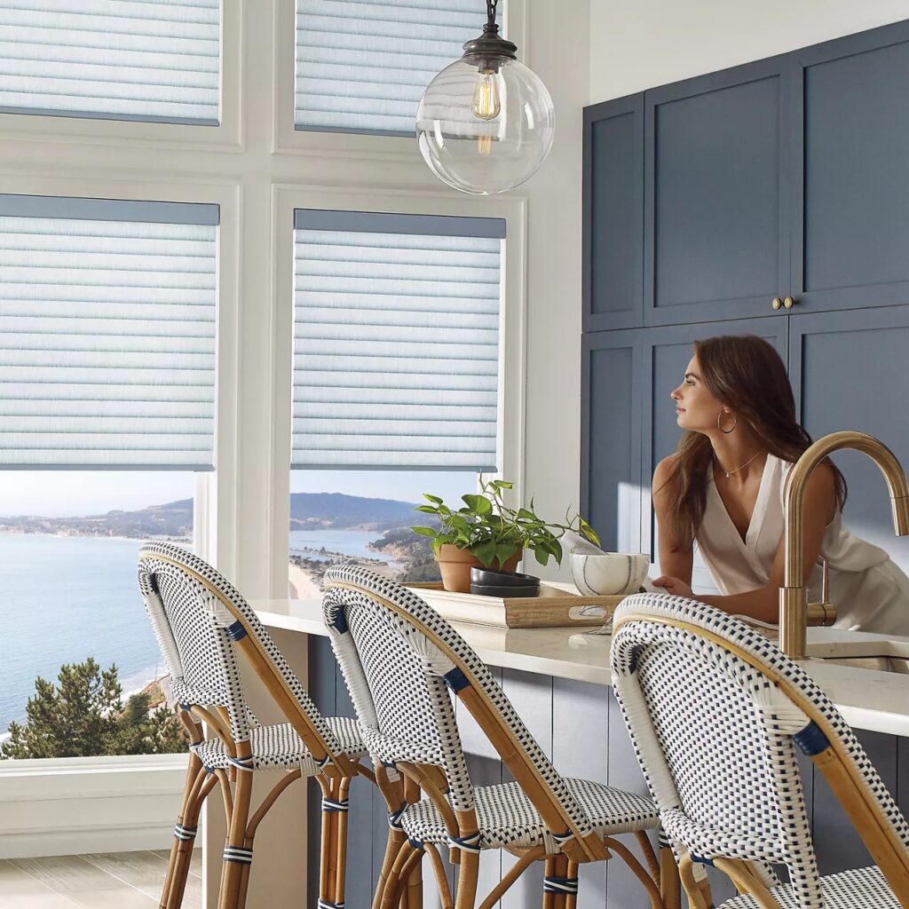 A woman leaning over a kitchen counter. The kitchen windows are partially covered by motorized blinds.