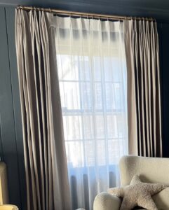 A sheer curtain covering a room window. It is layered beneath another window treatment.