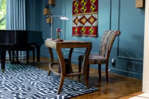 Draped in Style, Louisville’s trusted custom drapery experts, present cozy study with wooden desk, striped chair, geometric rug, and grand piano.