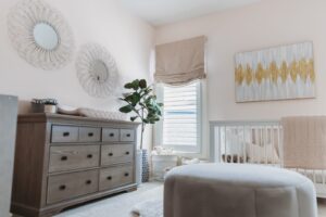 Louisville nursery with custom draperies, crib, wooden dresser, soft bedding, and gold-accented art by Draped in Style—trusted for timeless style.